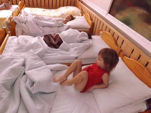 Девочка в красной маечке на кроватке делает упражнения