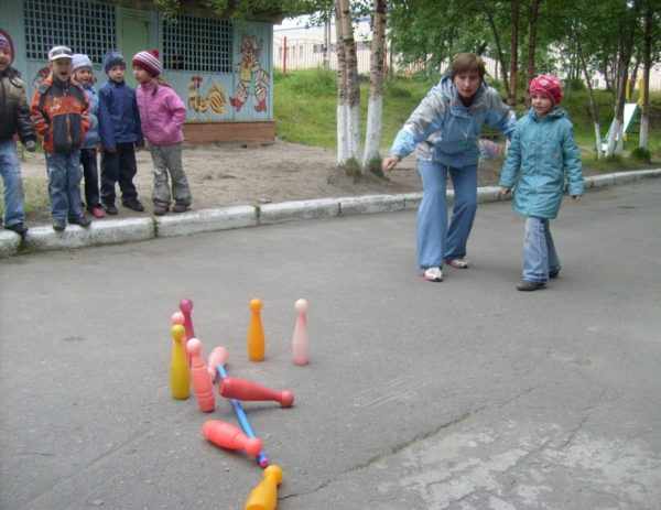 Дети и воспитатель играют на улице в кегли