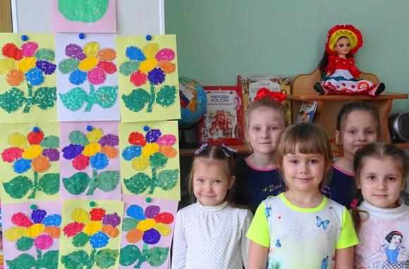 Девочки стоят рядом со стендом с аппликациями цветов