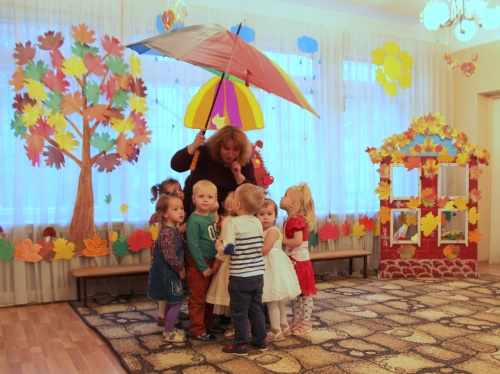 Воспитательница держит зонт и что-то рассказывает детям