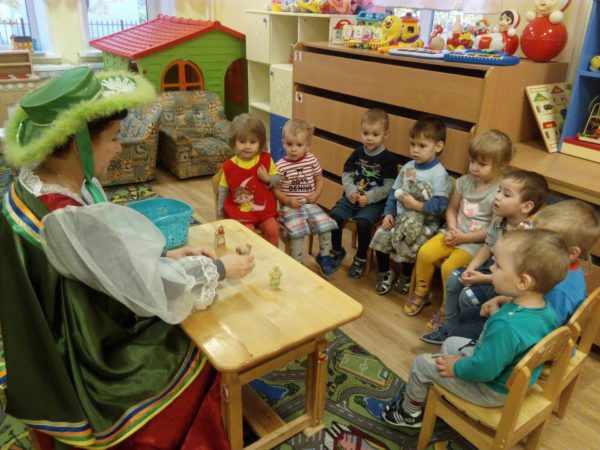 Воспитательница в костюме показывает детям маленьких кукол