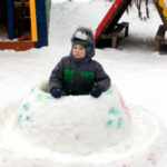 Ребёнок сидит в летающей тарелке, сделанной из снега