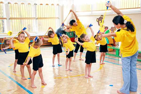 Дети с педагогом делают наклоны с гимнастической палкой