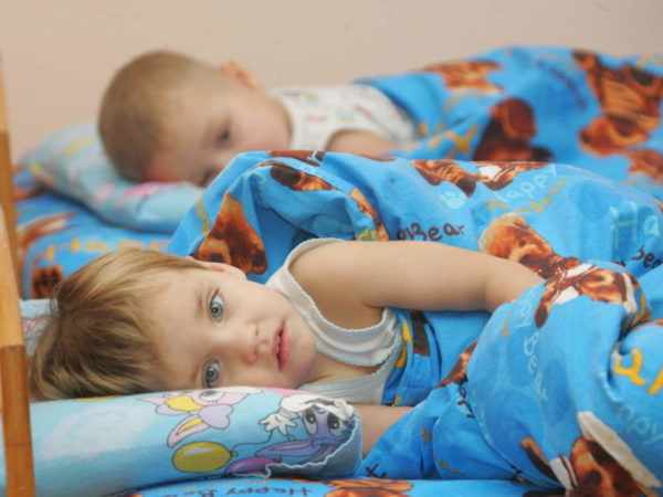 Два ребёнка не спят, лёжа в кровати, во время тихого часа