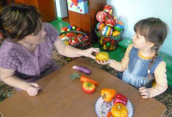 Воспитательница показывает на картофелину, которую держит девочка