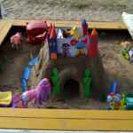 Дворец с башнями в песочнице, вокруг небольшие игрушки