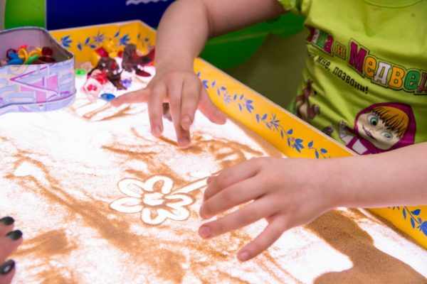 Ребёнок создаёт изображение цветка с помощью песка