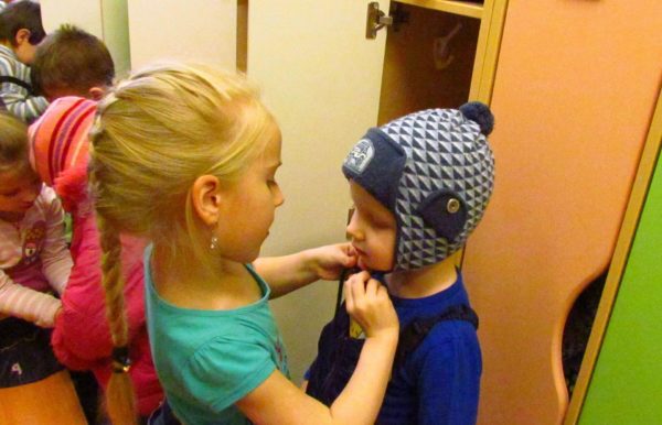 Девочка помогает маленькому мальчику надеть шапку
