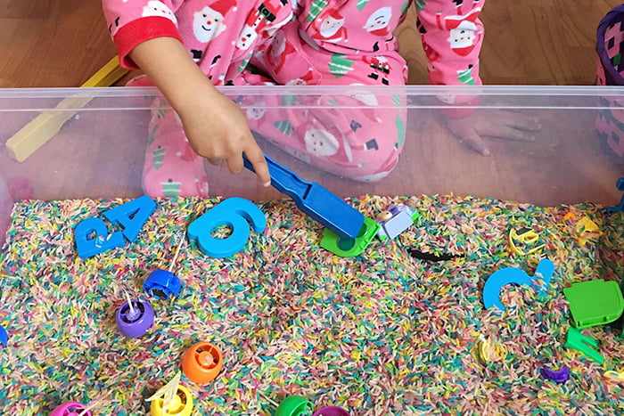 Ребенок играет с сенсорной коробкой, наполненной крупой и игрушками
