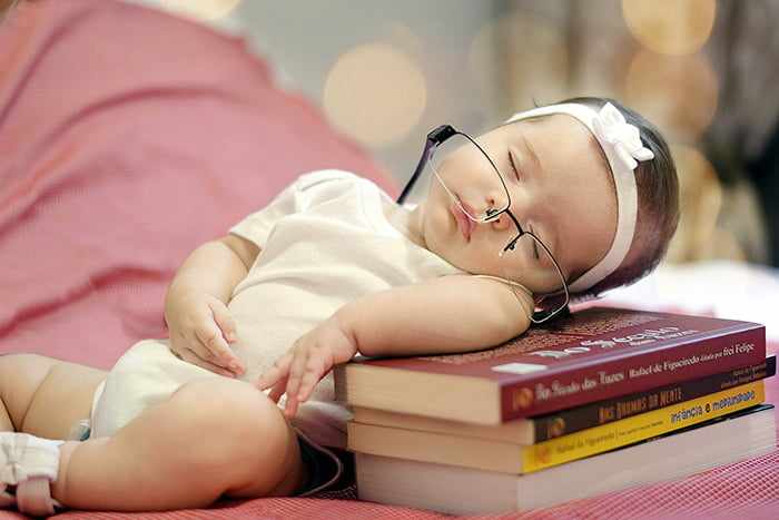 Трехмесячная девочка спит на стопке книг