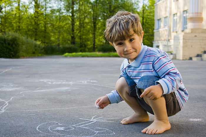 Четырехлетний мальчик рисует на асфальте