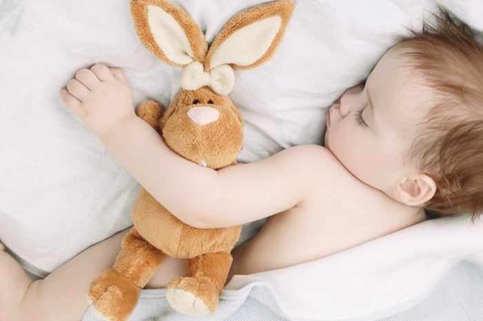 Годовалый ребенок спит с плюшевым зайцем