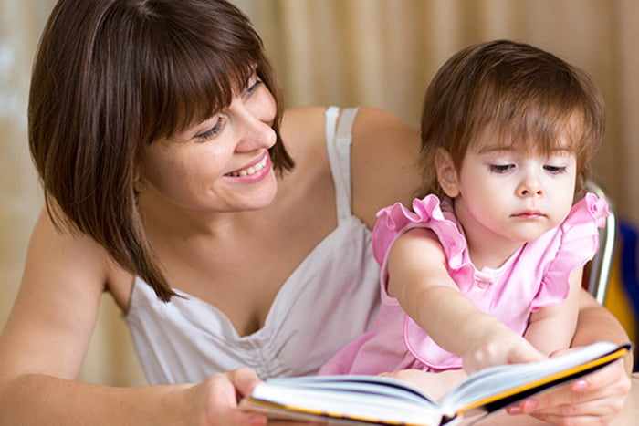 Маленькая девочка рассматривает книжку на руках у мамы